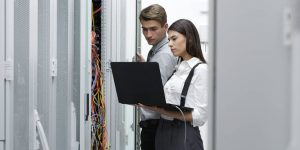 парень с девушкой в дата центре хостинг провайдера и анализируют на ноутбуке работу серверов на Windows